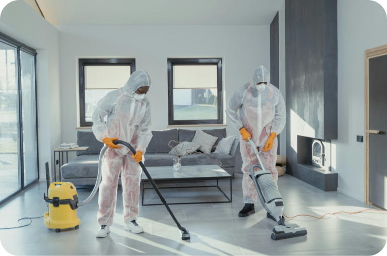 Two people in full protective suits, possibly cleaning professionals, vacuuming a modern living room. The image suggests a deep cleaning or sanitation service.